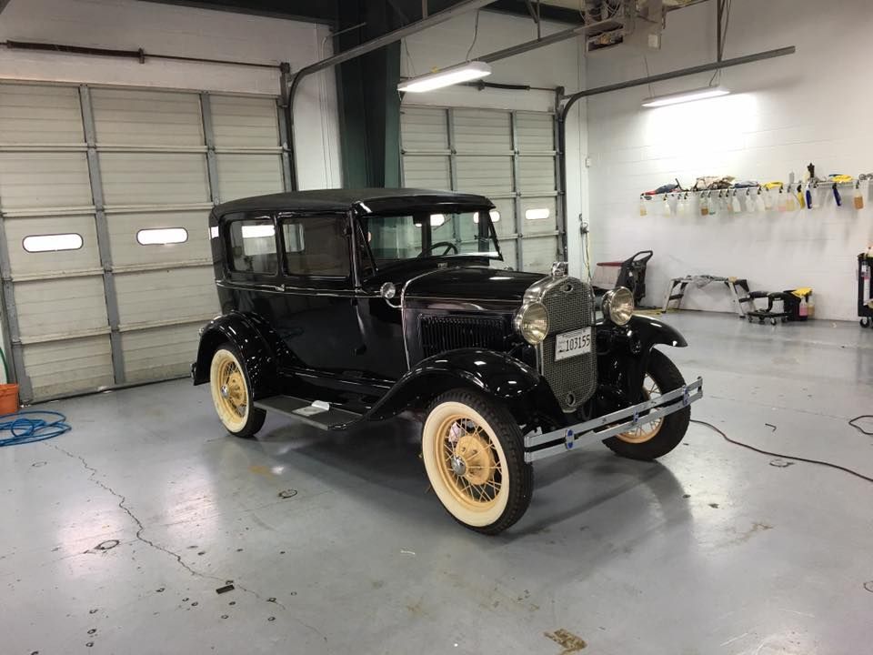 An old black car is parked in a garage next to a garage door.