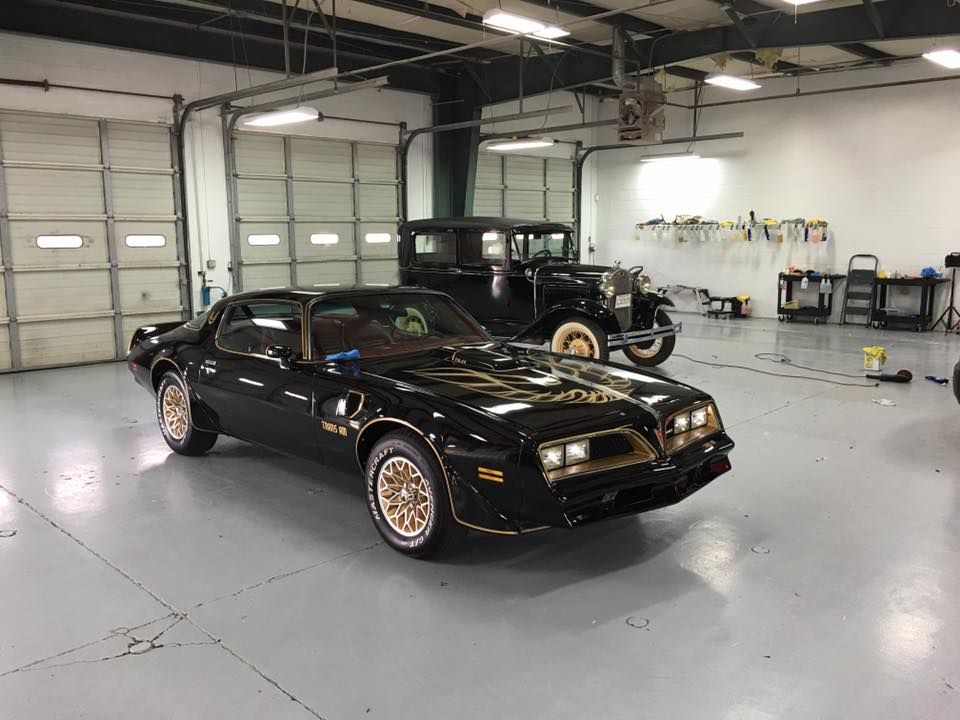 A black car is parked in a garage next to an old car.