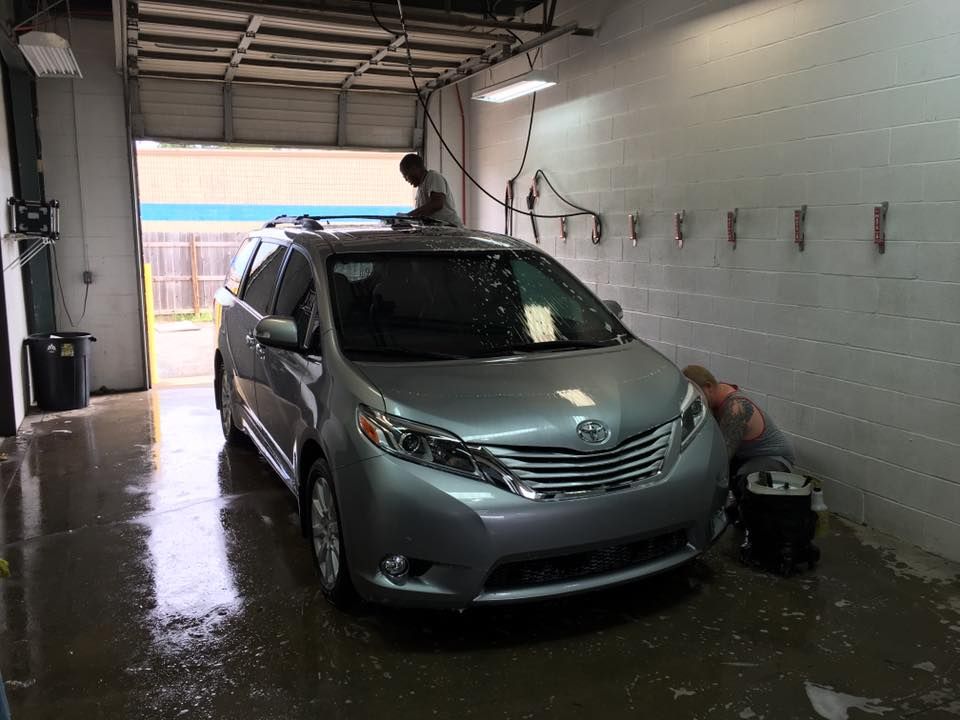 A silver minivan is being washed in a car wash.