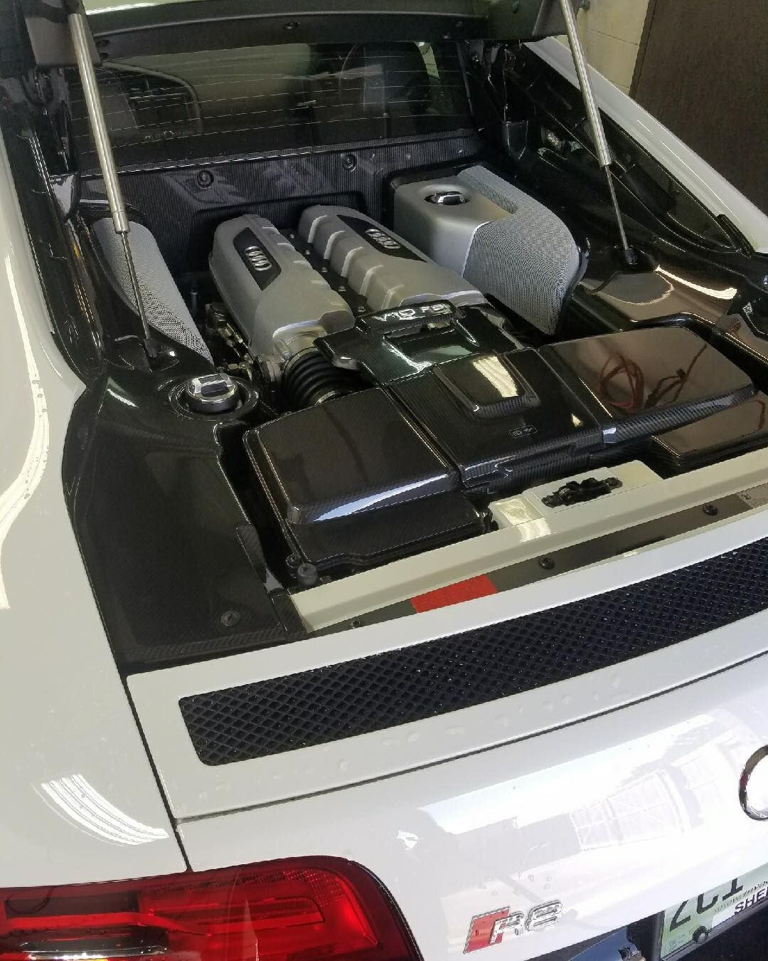 The trunk of a white sports car is open and shows the engine.