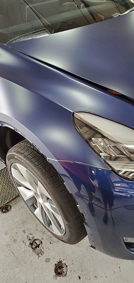 A blue car is parked in a garage with the hood up.