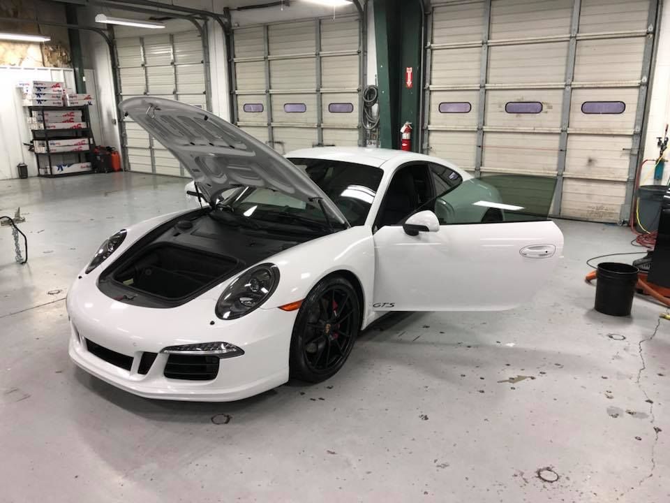 A white porsche 911 gt3 is parked in a garage with its hood up.