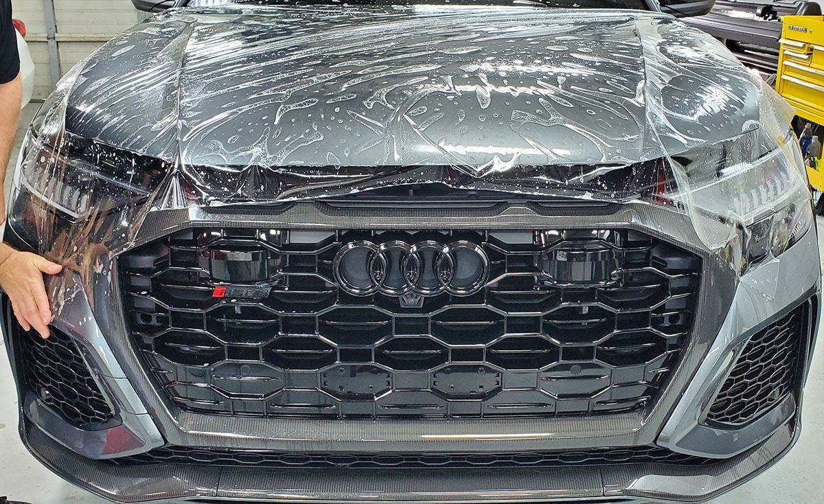 A person is covering the front of a car with plastic wrap.