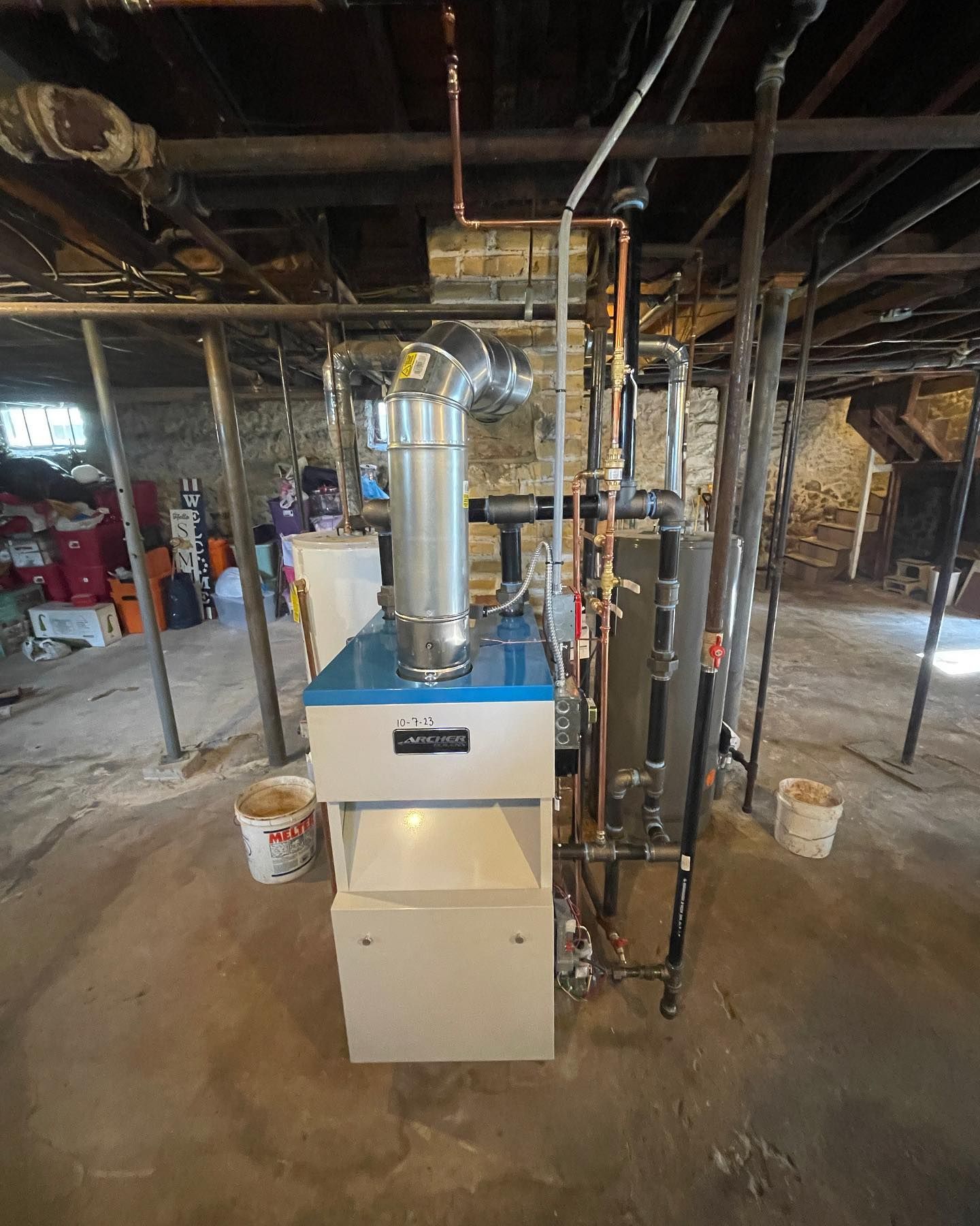 A blue and beige residential furnace with metal venting and copper piping stands in a concrete basement.
