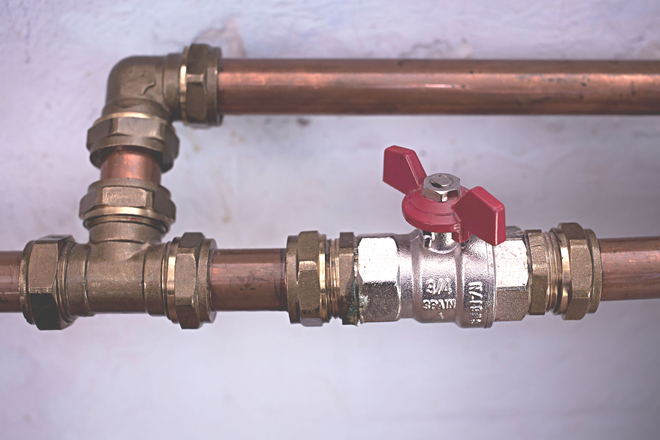 A section of copper plumbing pipe with a T-joint, elbow, and a ball valve with a red handle.
