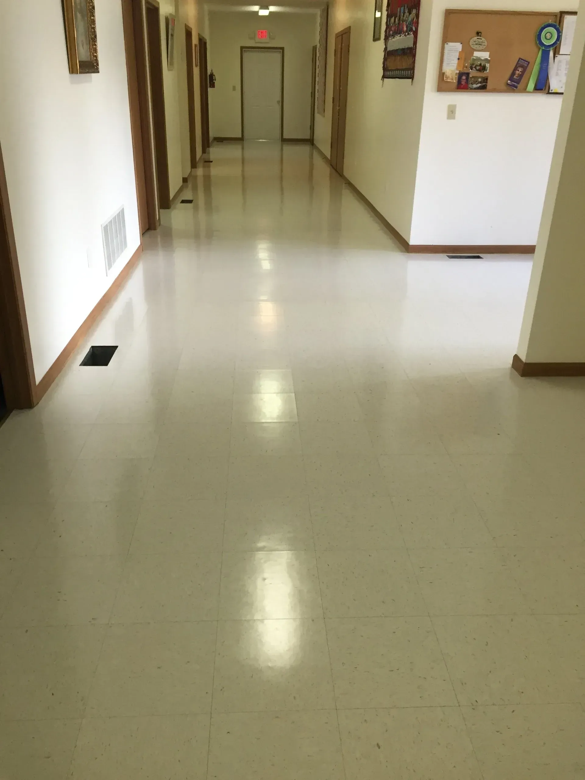 Long, empty hallway with glossy, off-white floor and doors on both sides.