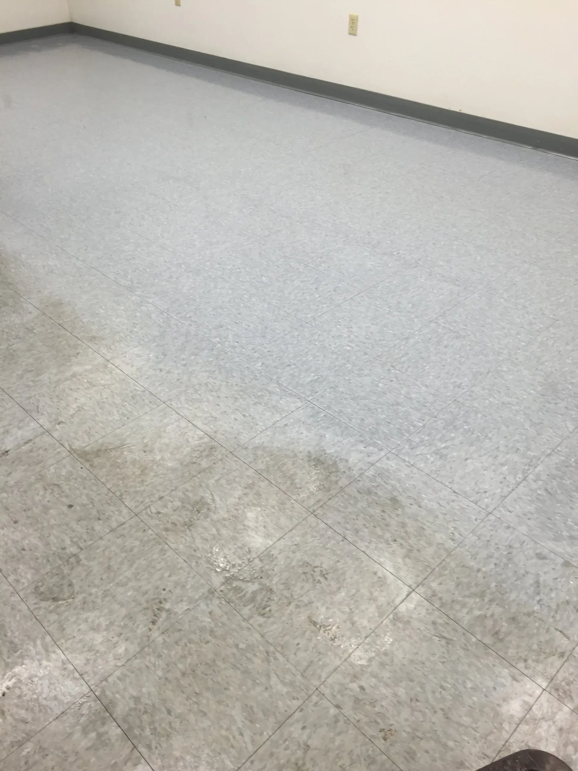 Gray speckled linoleum floor in a room with white walls and a dark gray baseboard.