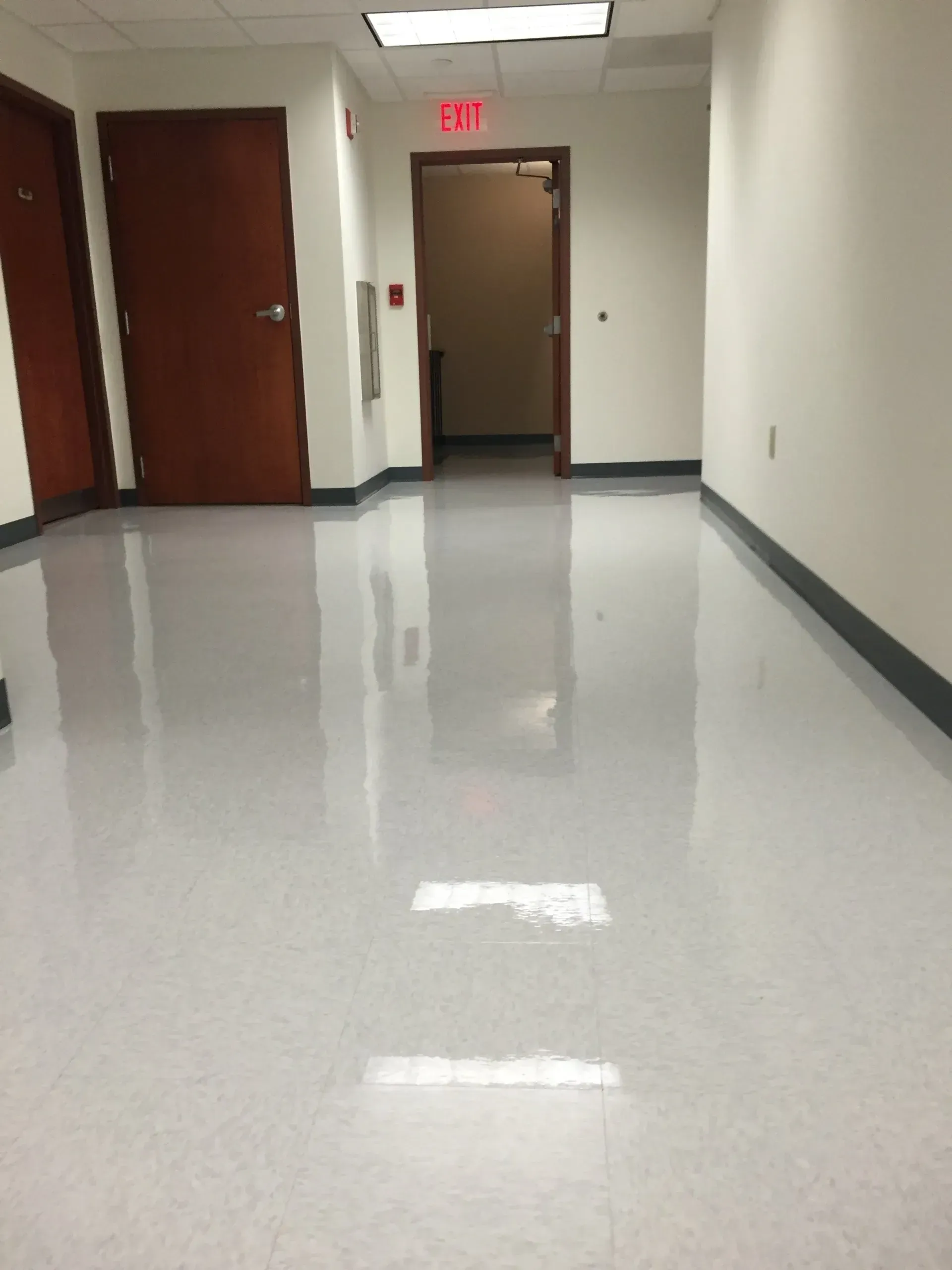Hallway with polished white floor, brown doors, and an exit sign.