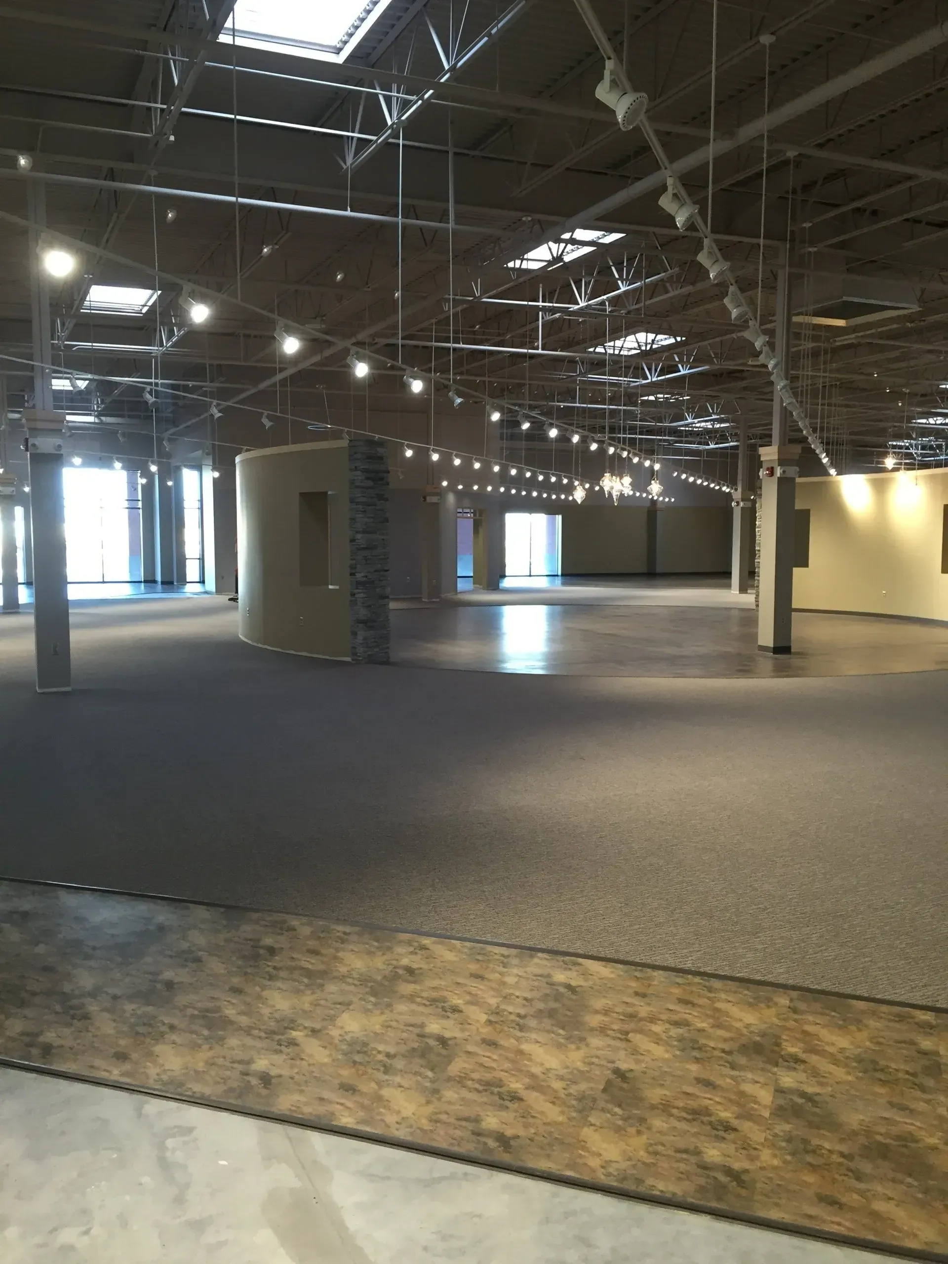 Empty warehouse interior with concrete floor and dark carpet. Metal beams and lights visible on ceiling.