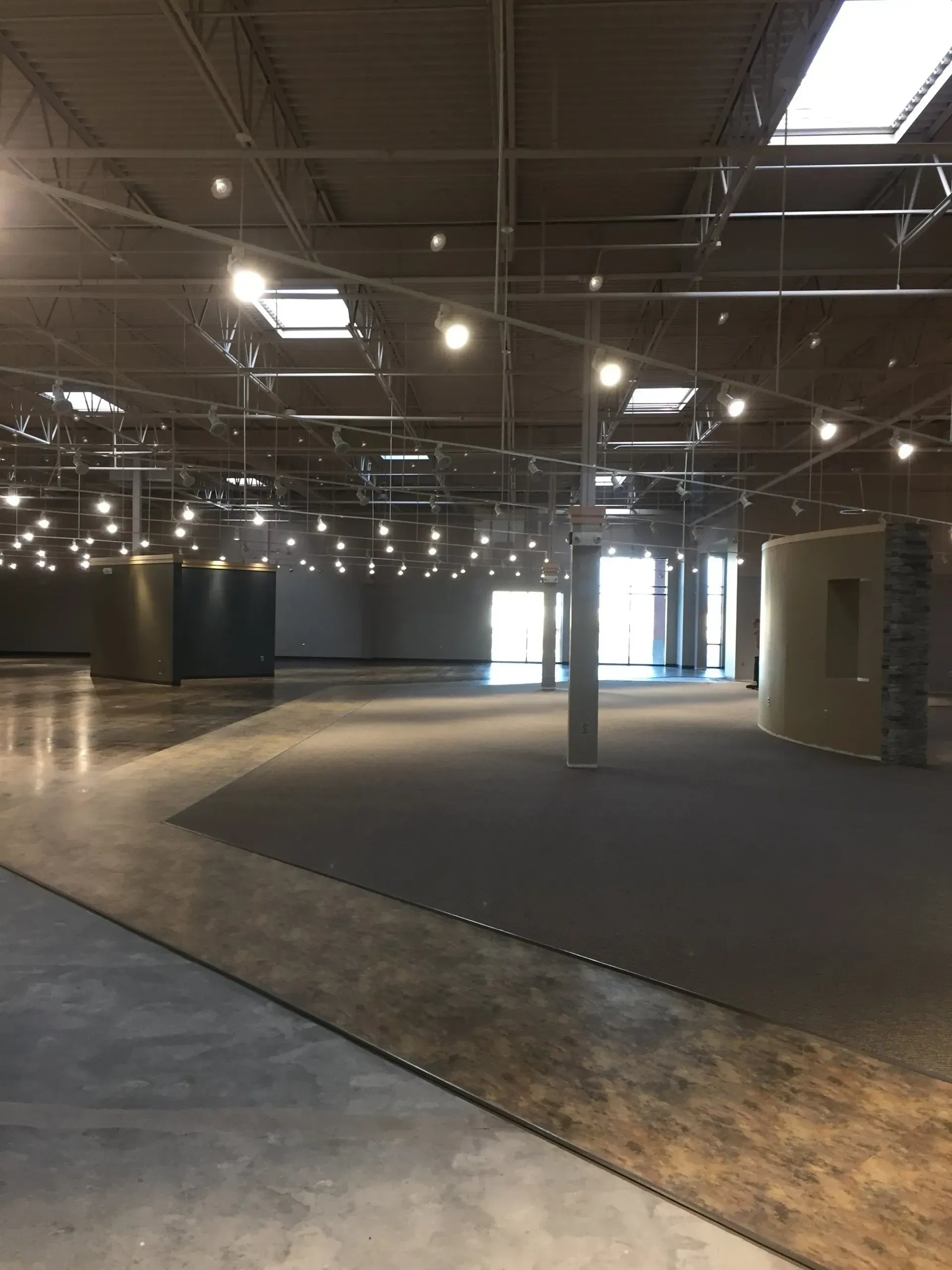 Empty, modern retail space with polished concrete floors, track lighting, and a dark gray carpeted section.