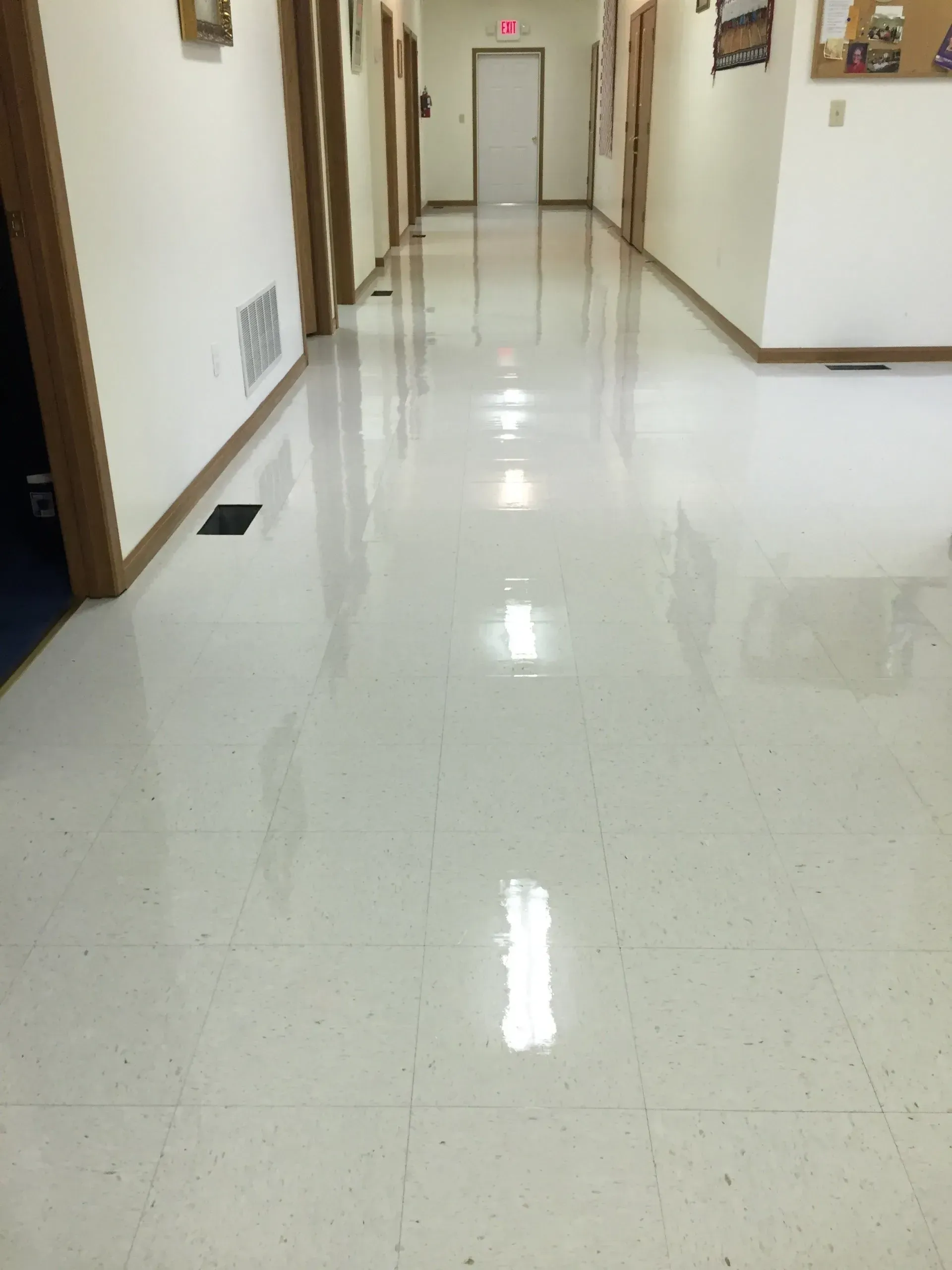A long, bright hallway with shiny white tiled floor and doors on either side.