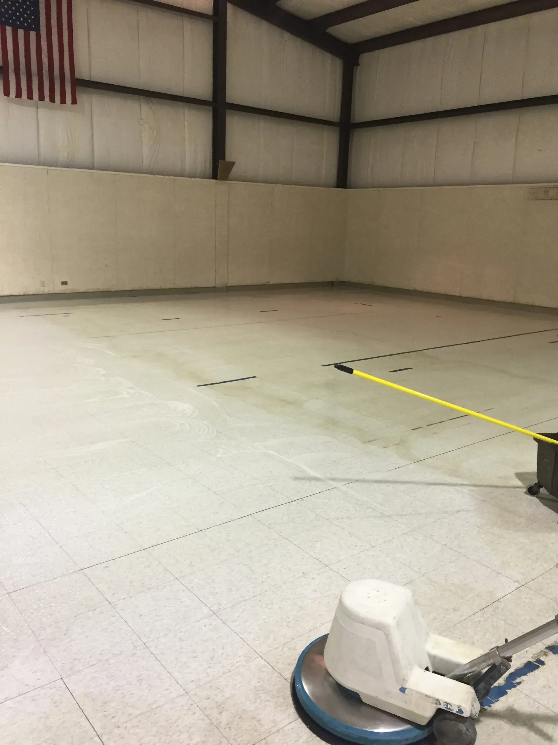 A floor buffer cleaning a large, empty room with an American flag on the wall.