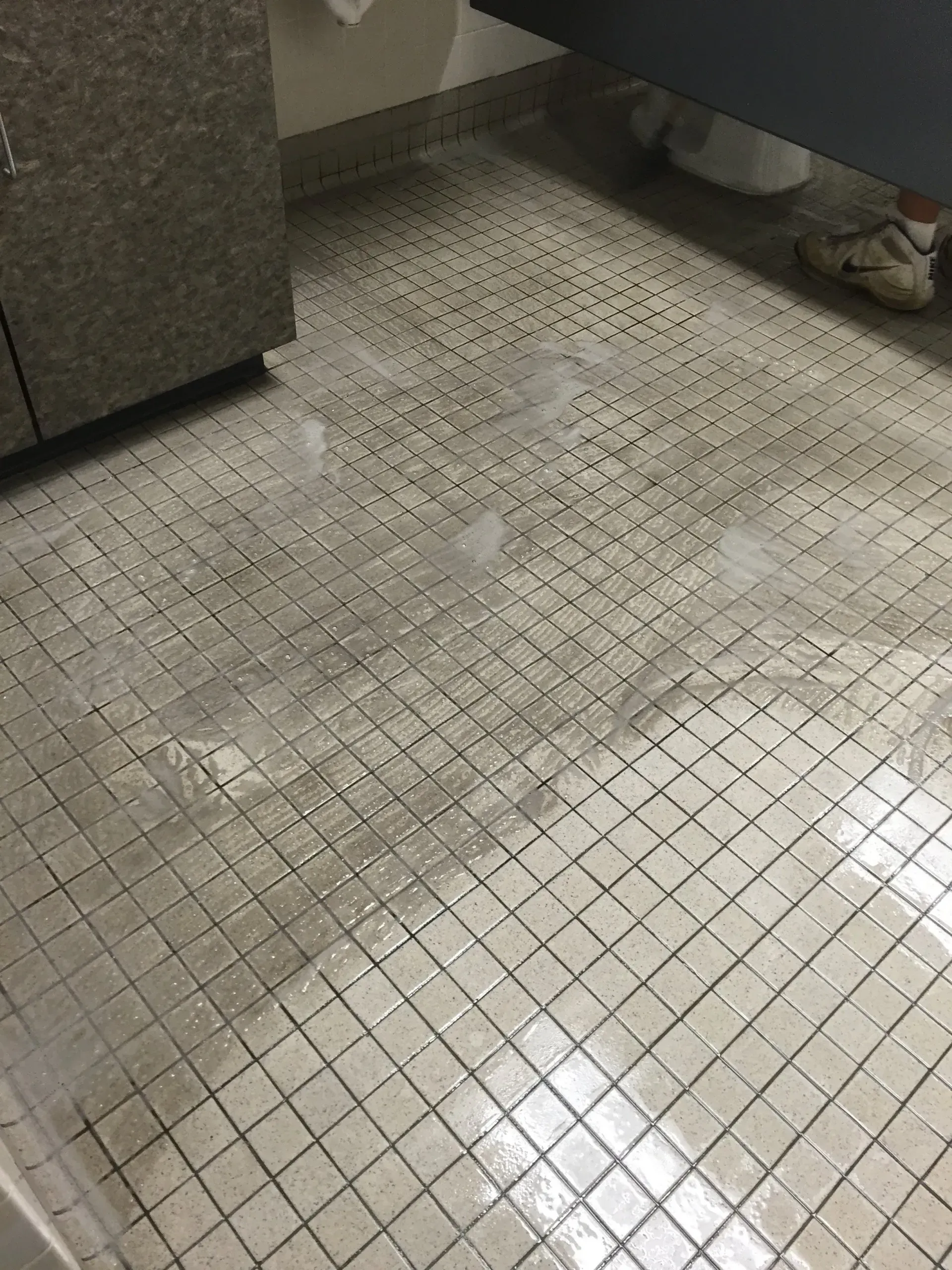 Wet, tiled floor in a public restroom. Surface is slick, potentially hazardous.