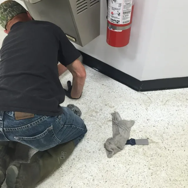 Person kneeling on floor near a wall, cleaning something. Fire extinguisher hangs on wall.