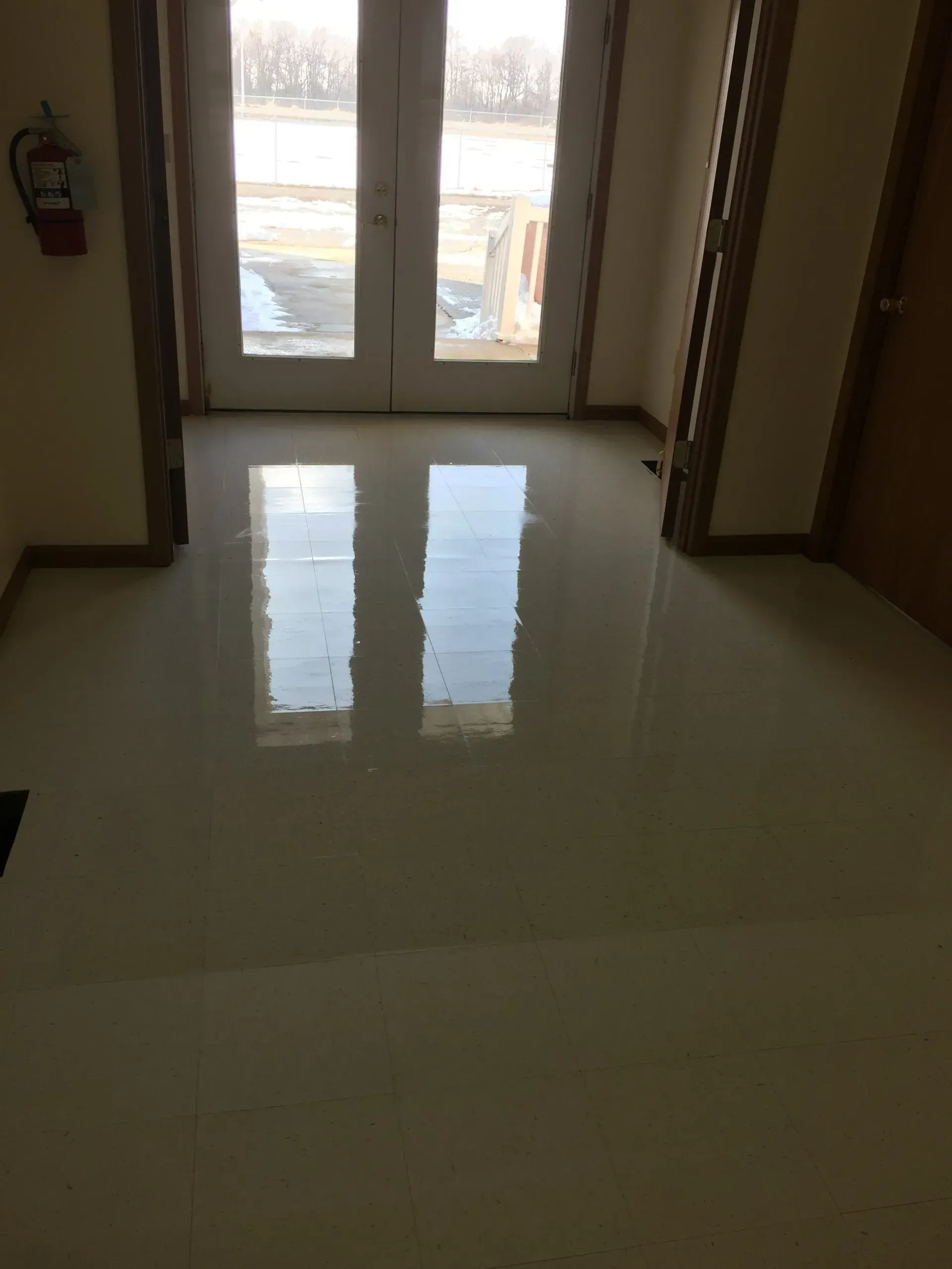 Interior doorway with white doors reflecting light on a shiny, light-colored floor. Fire extinguisher on the wall.
