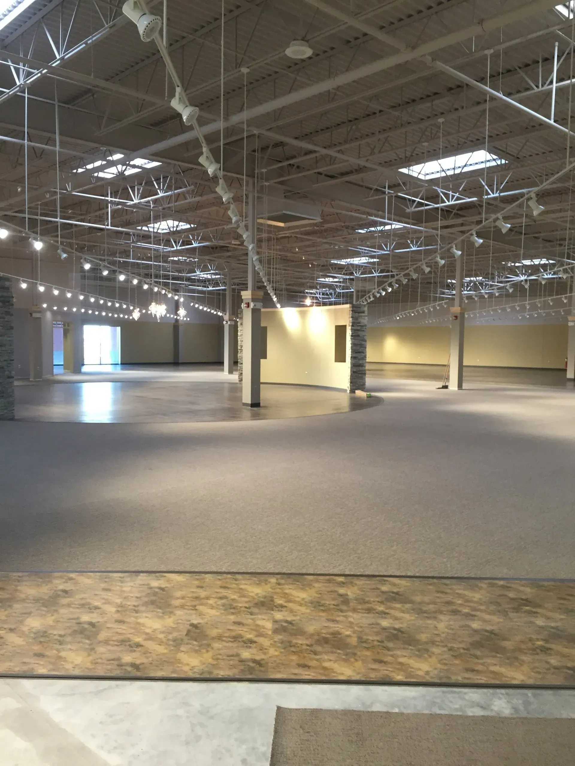 Large, empty commercial interior with a high ceiling, concrete floor, and overhead lighting.