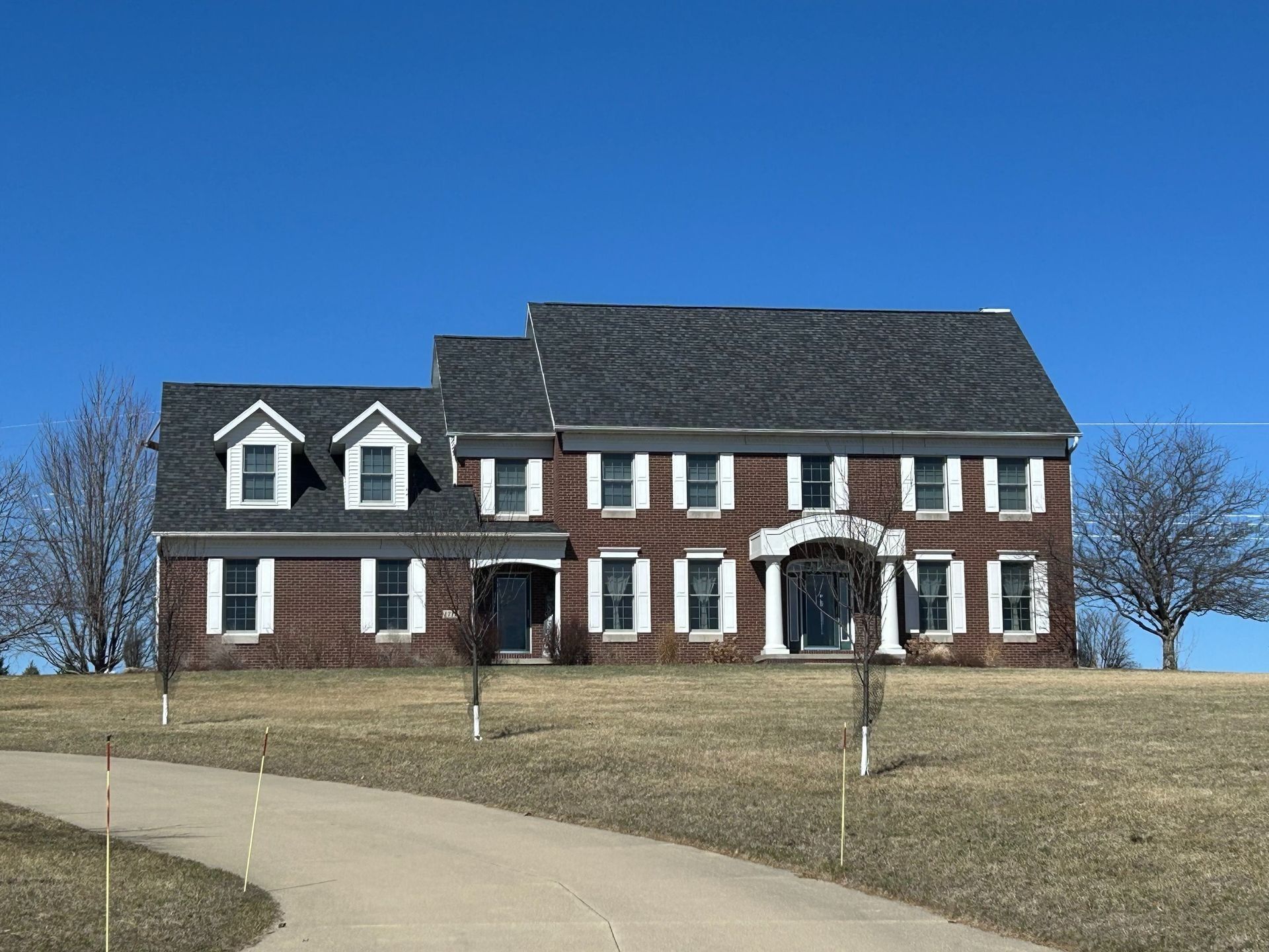 Red brick house on a hill, blue sky, white shutters, driveway leading up.