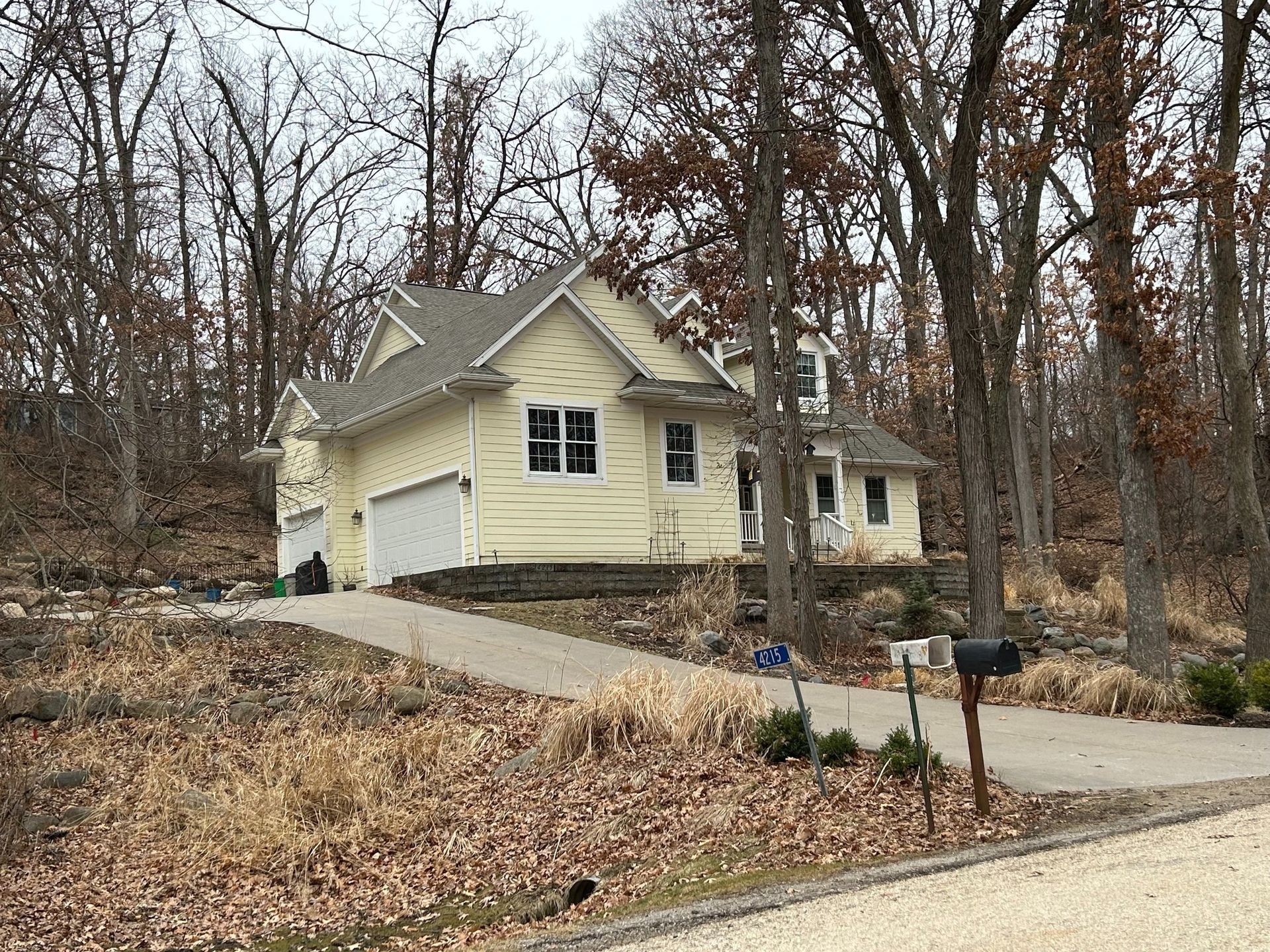 Yellow house with driveway, mailbox, and trees in a wooded area.
