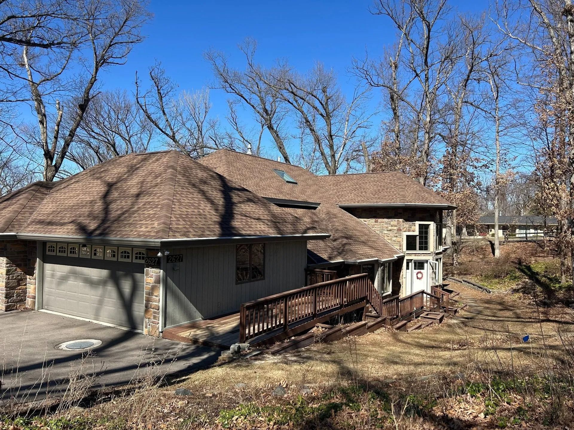 House with garage, brown roof, and wooden ramp in a wooded setting under a clear blue sky.