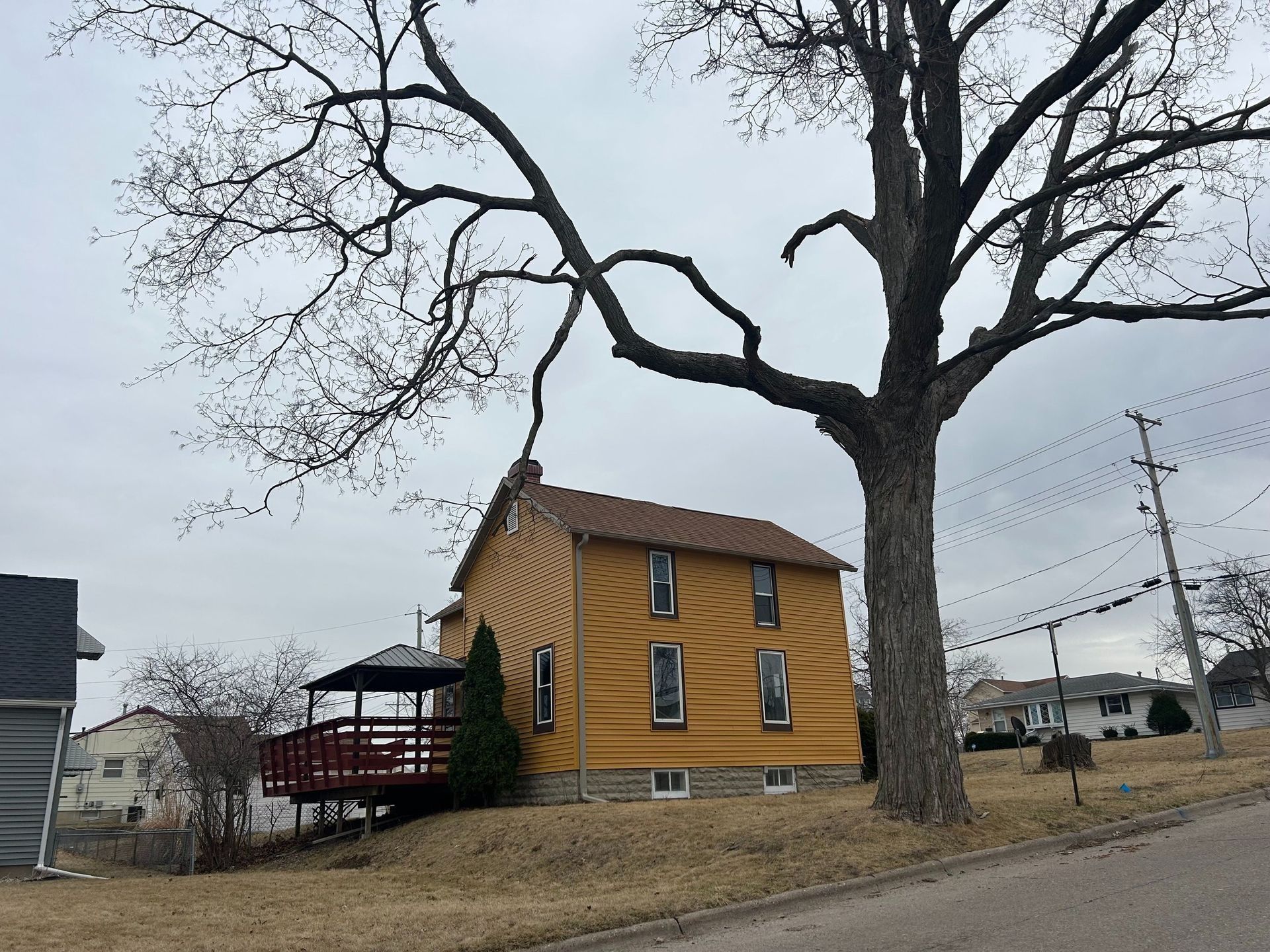 Yellow house with red porch, large bare tree, cloudy sky.