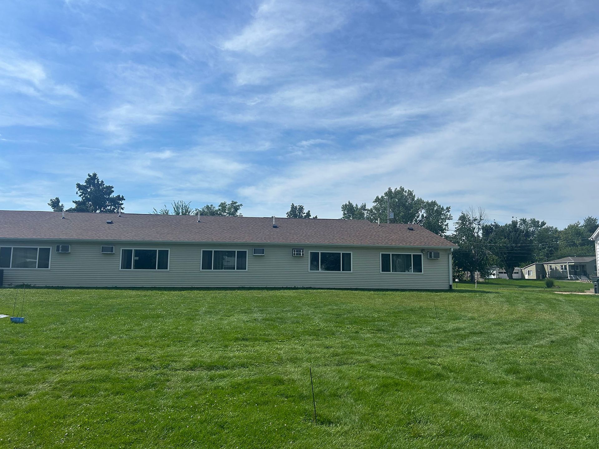 A long, one-story building with a brown roof and multiple windows under a partly cloudy sky.