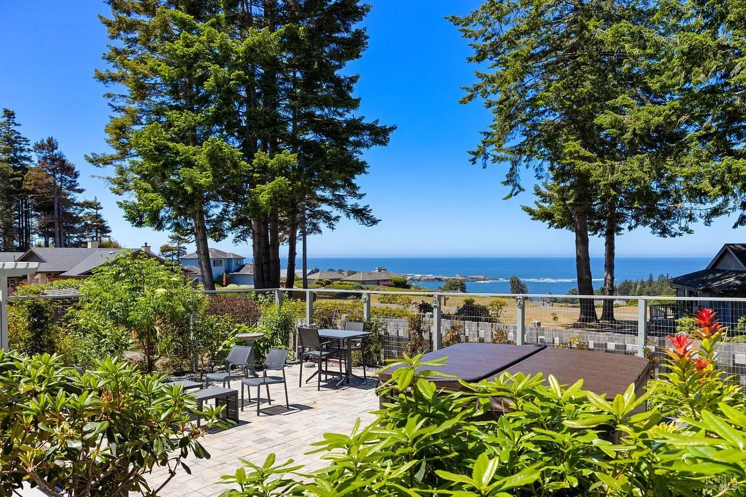 a patio with tables and chairs and a hot tub with a view of the ocean