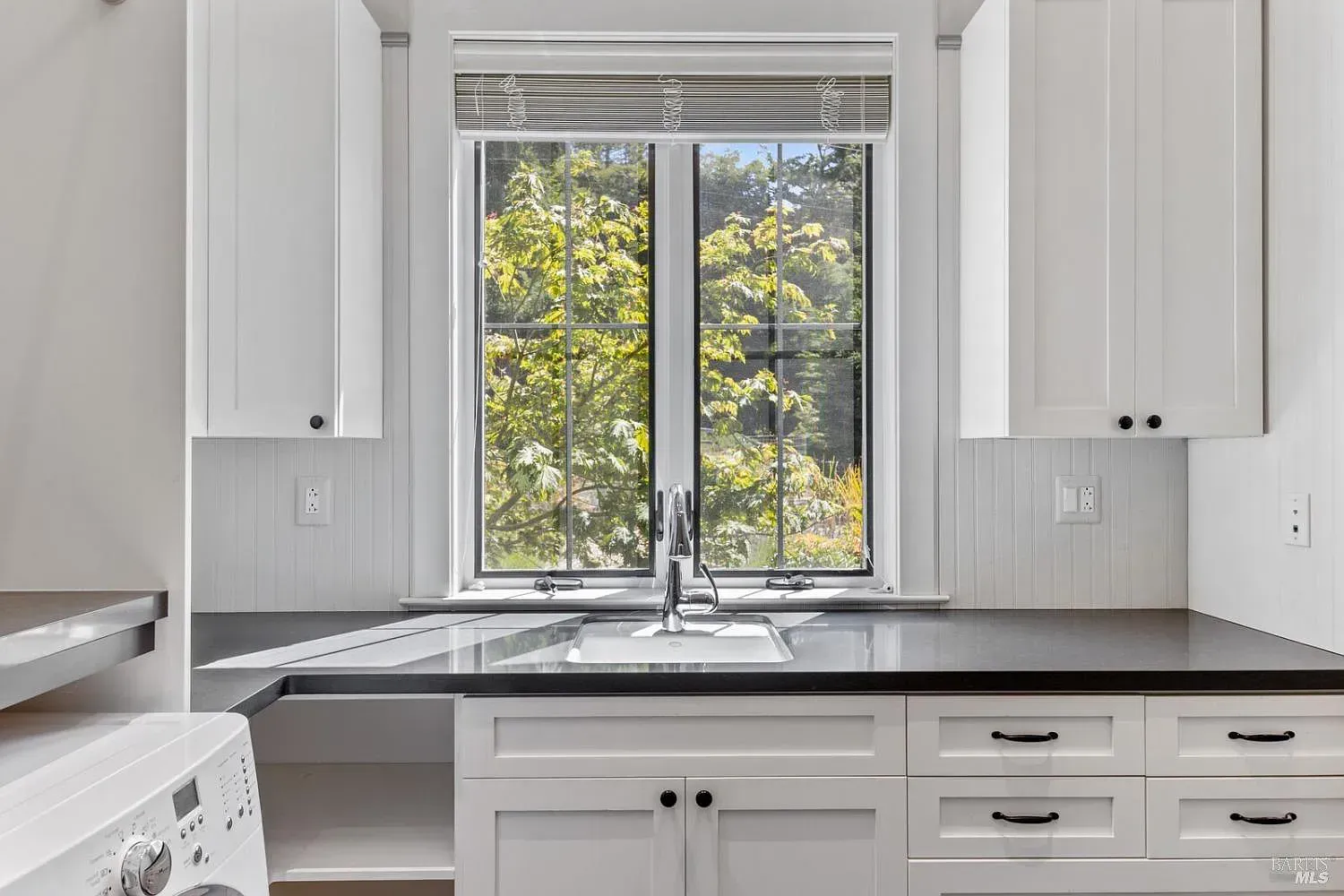 a kitchen with white cabinets, black counter tops, a sink, and a window