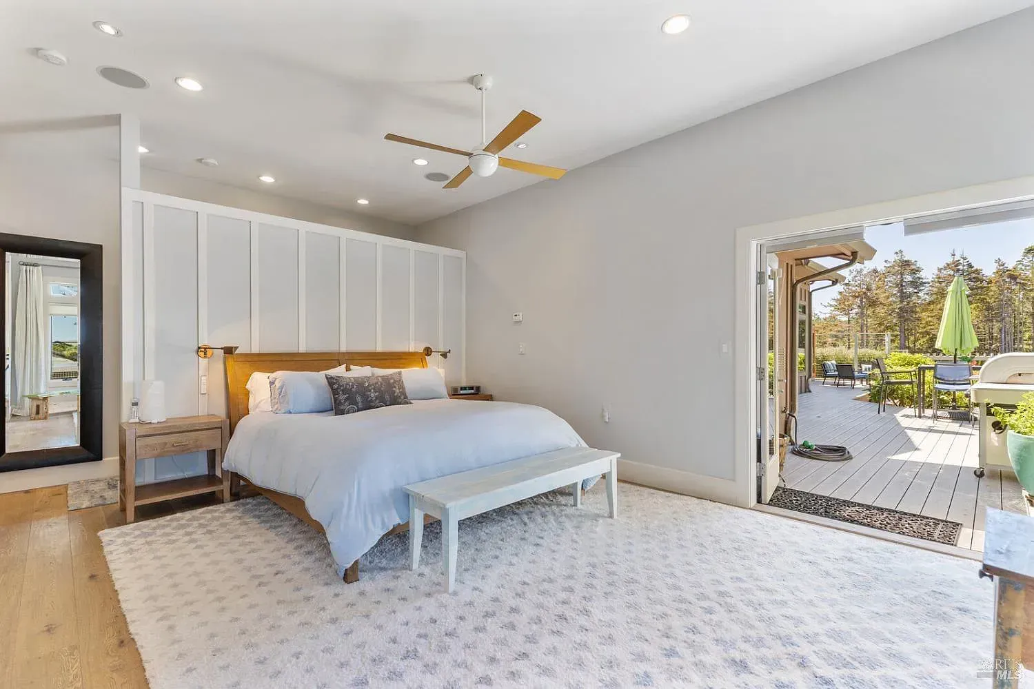 a bedroom with a large bed, a bench, a mirror, and a ceiling fan