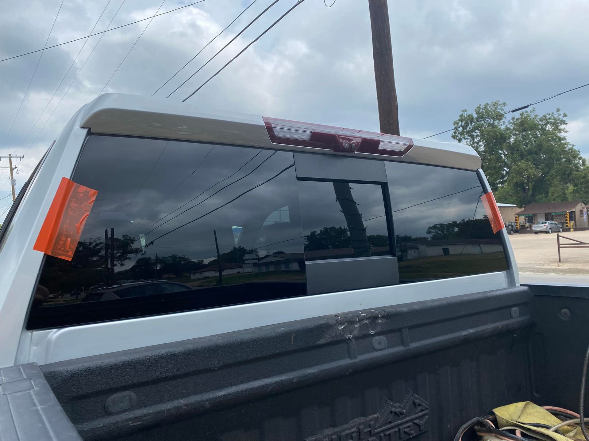 Silver pickup truck rear window with orange parking permit, parked on a street under cloudy sky