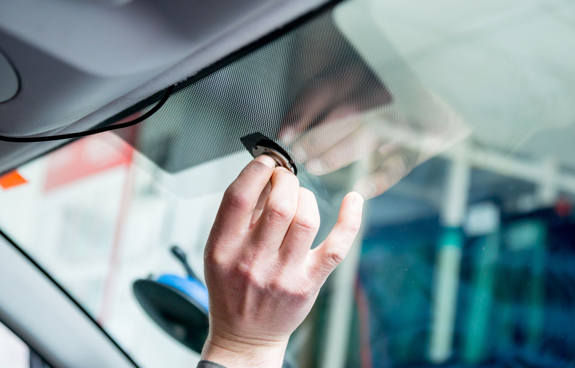 Hand wiping a car windshield with a cloth near the rearview mirror and dashboard