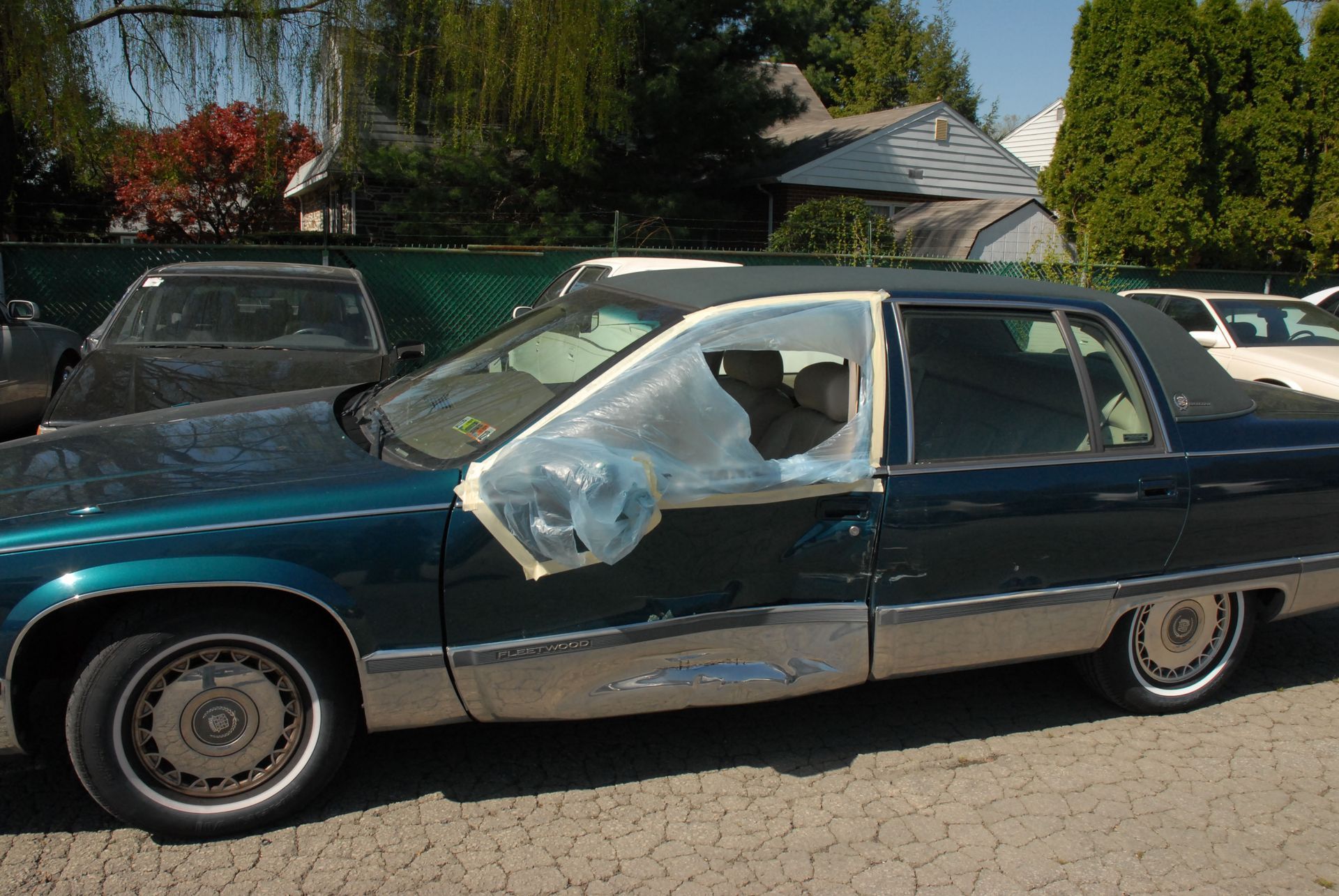 Dark green classic car with a badly damaged windshield and front window, parked outdoors