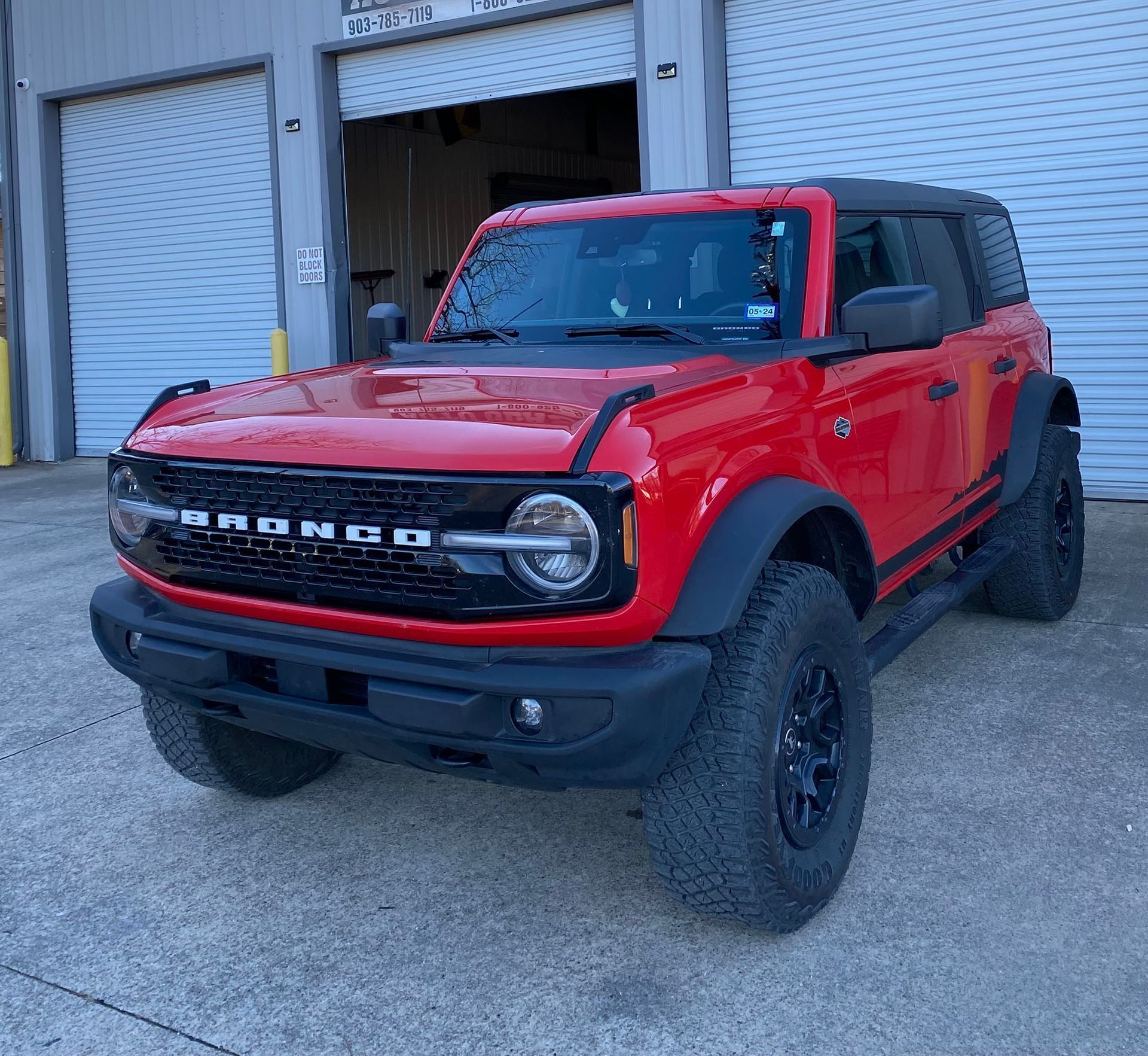 Red Ford Bronco SUV parked outside a warehouse with roll-up doors