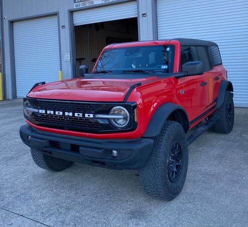 Red Ford Bronco SUV parked outside a warehouse with roll-up doors