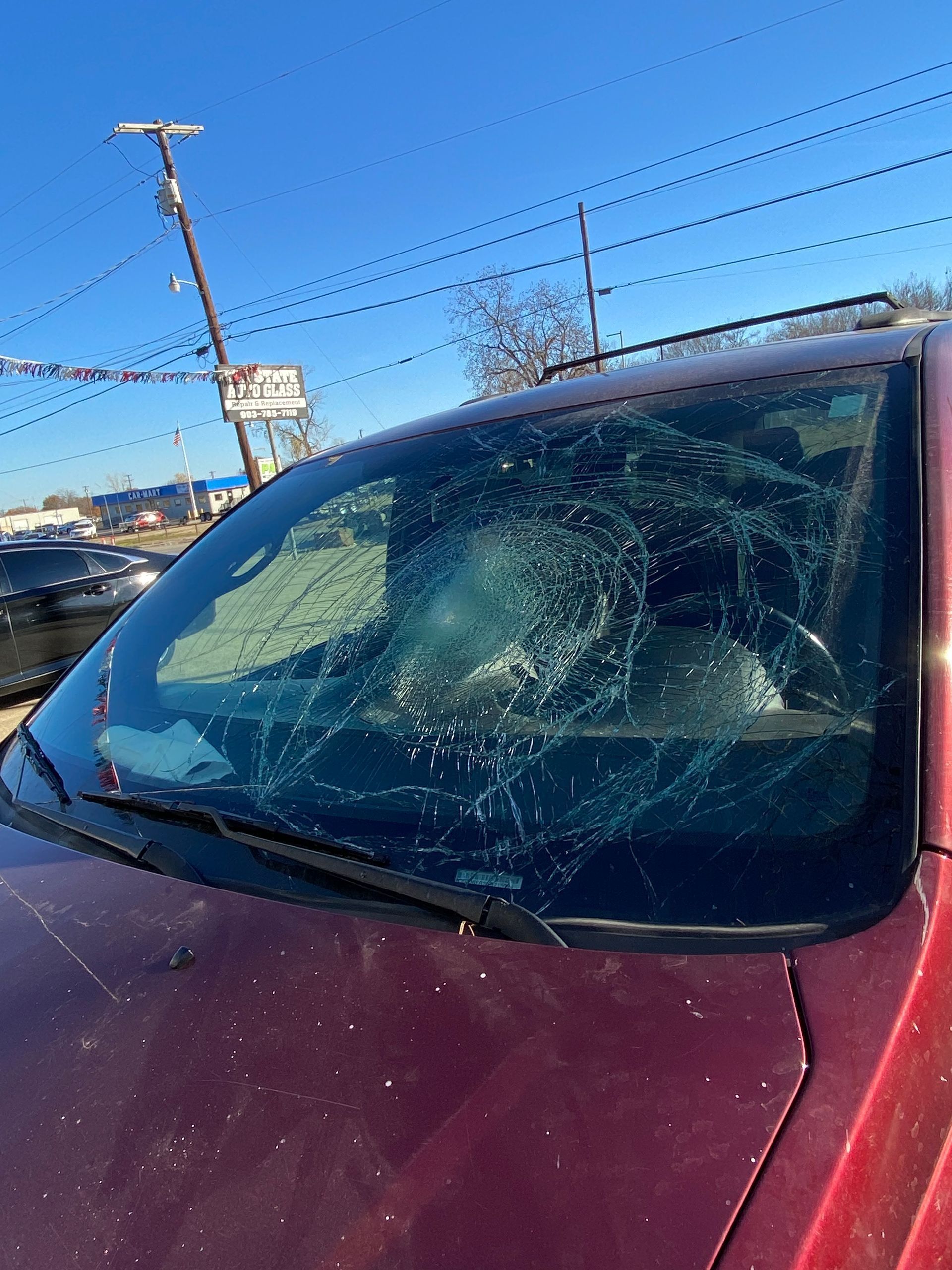 Red car windshield cracked and covered with ice in a sunny parking lot
