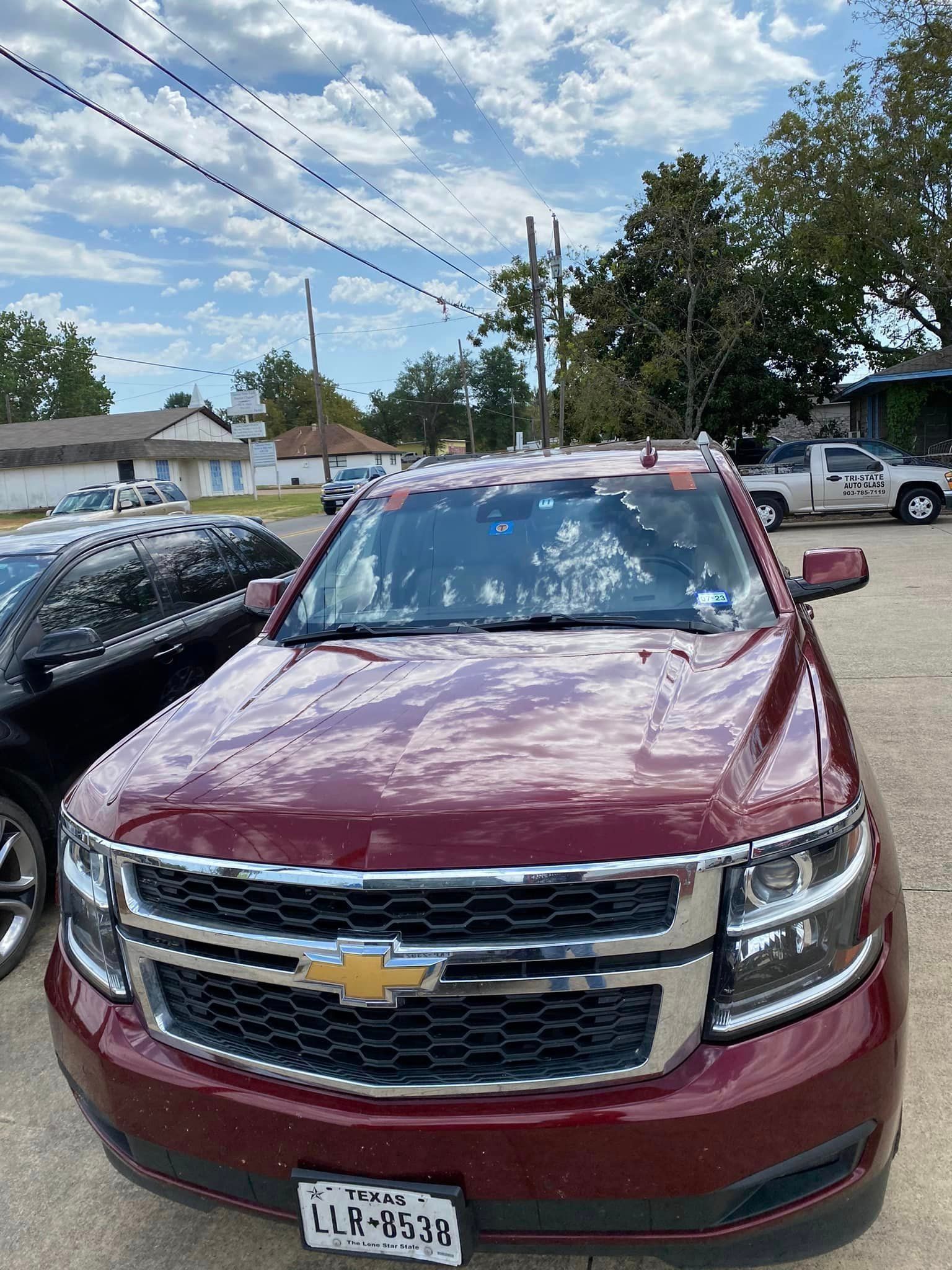 Maroon Chevrolet SUV parked outdoors in a lot under a cloudy sky, front view.