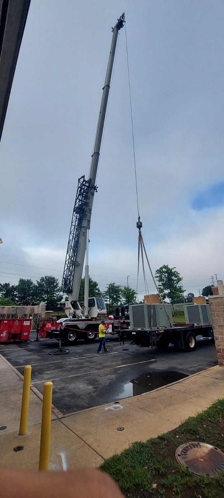 Crane and utility trucks lifting equipment at a wet outdoor worksite under a cloudy sky