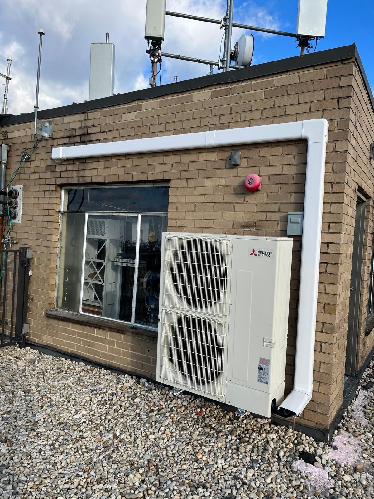 Rooftop HVAC unit with white ducting mounted on a tan brick building under a blue sky