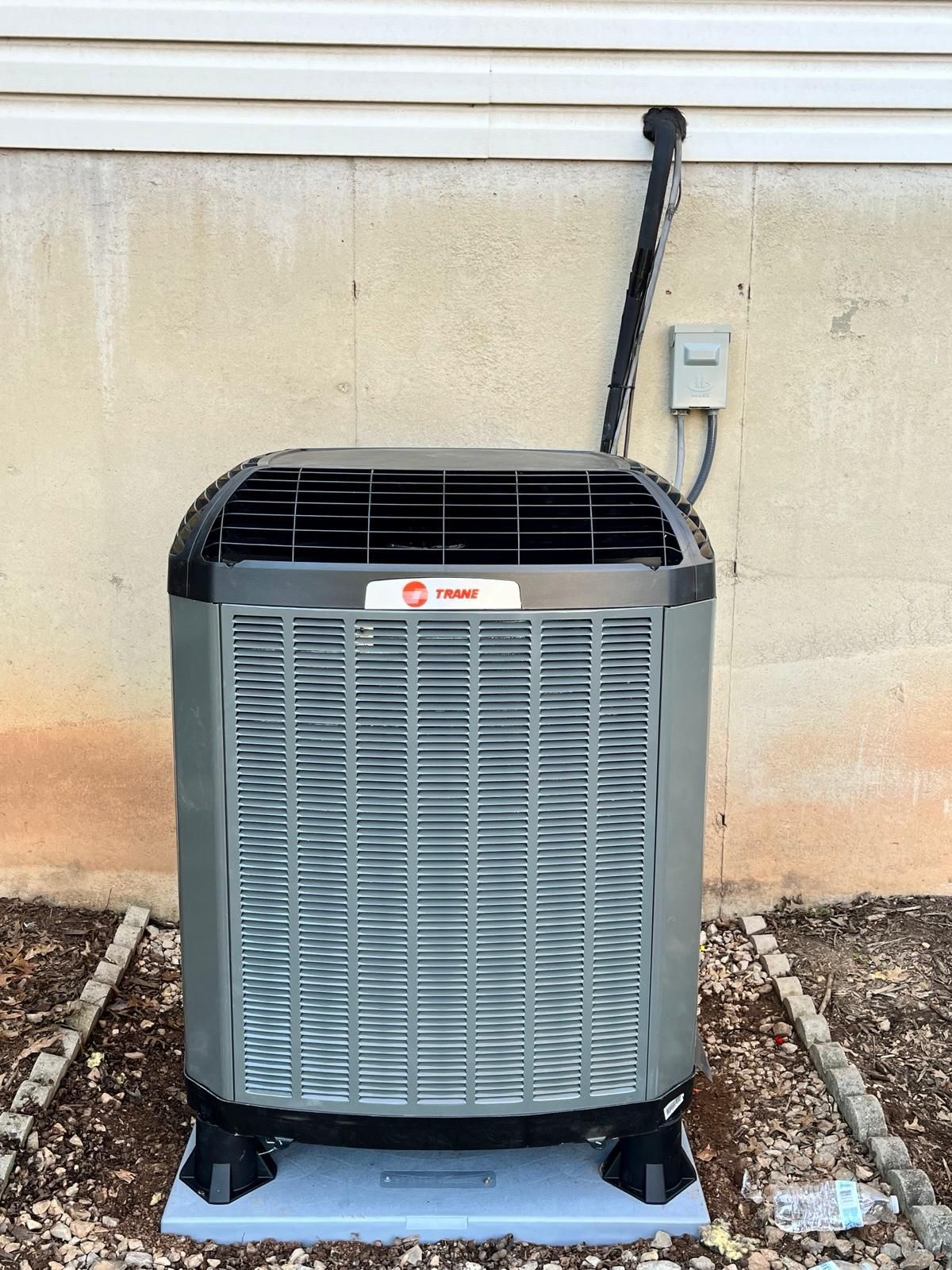 Outdoor HVAC condenser unit against a beige wall with black conduit and electrical box