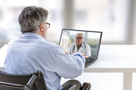 A man in a wheelchair is talking to a doctor on a laptop.