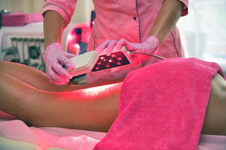 A woman is getting a red light treatment on her legs.