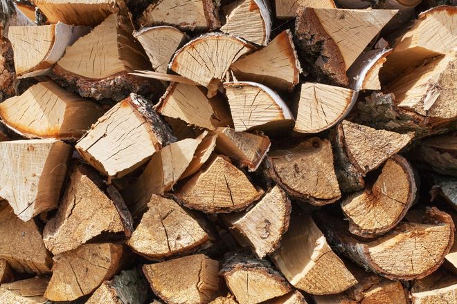 Pile of split firewood, various sizes, showing light brown wood grain, some with bark.