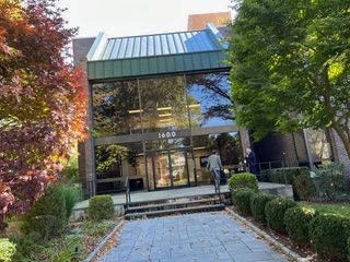 A two-story office building with a glass facade, a green metal roof, and a paved walkway leading to the entrance.