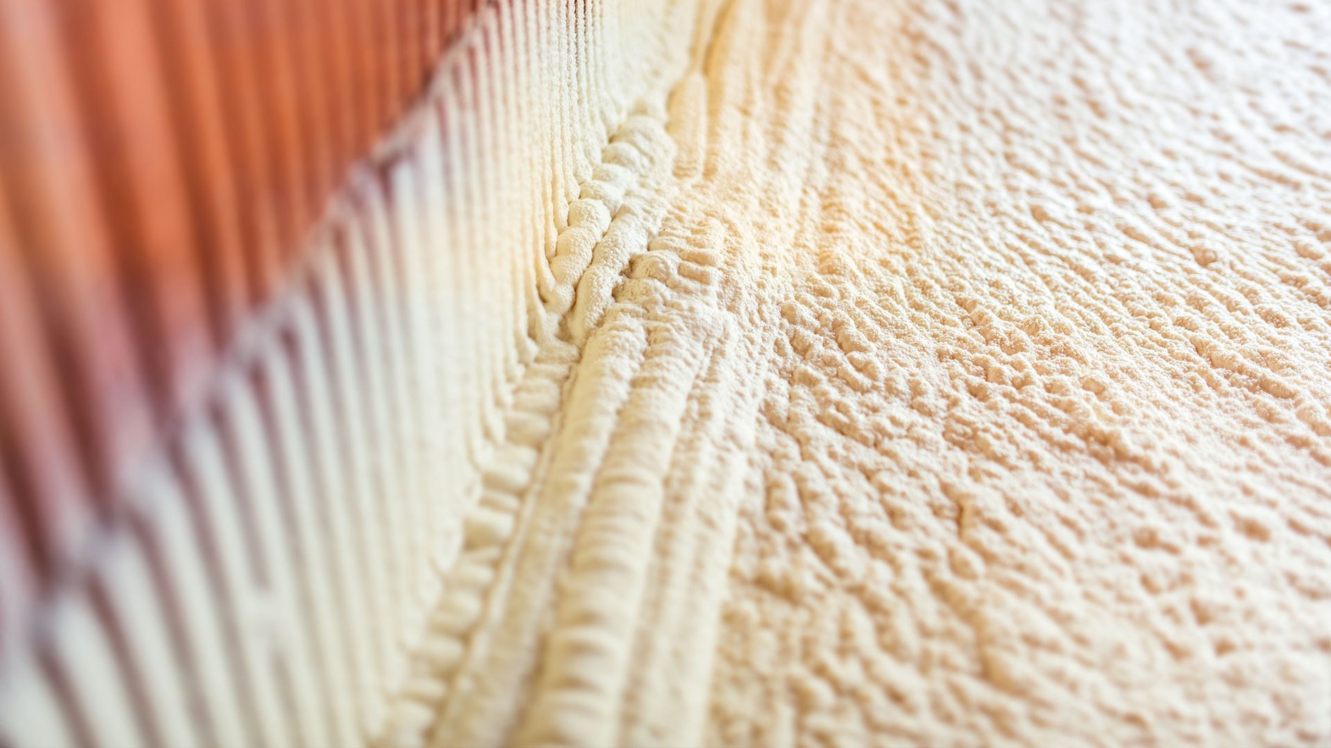 Beige spray foam insulation on a wall with orange paneling.