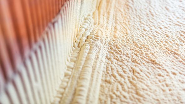 Spray foam insulation filling the space between a red wall and vertical beams.