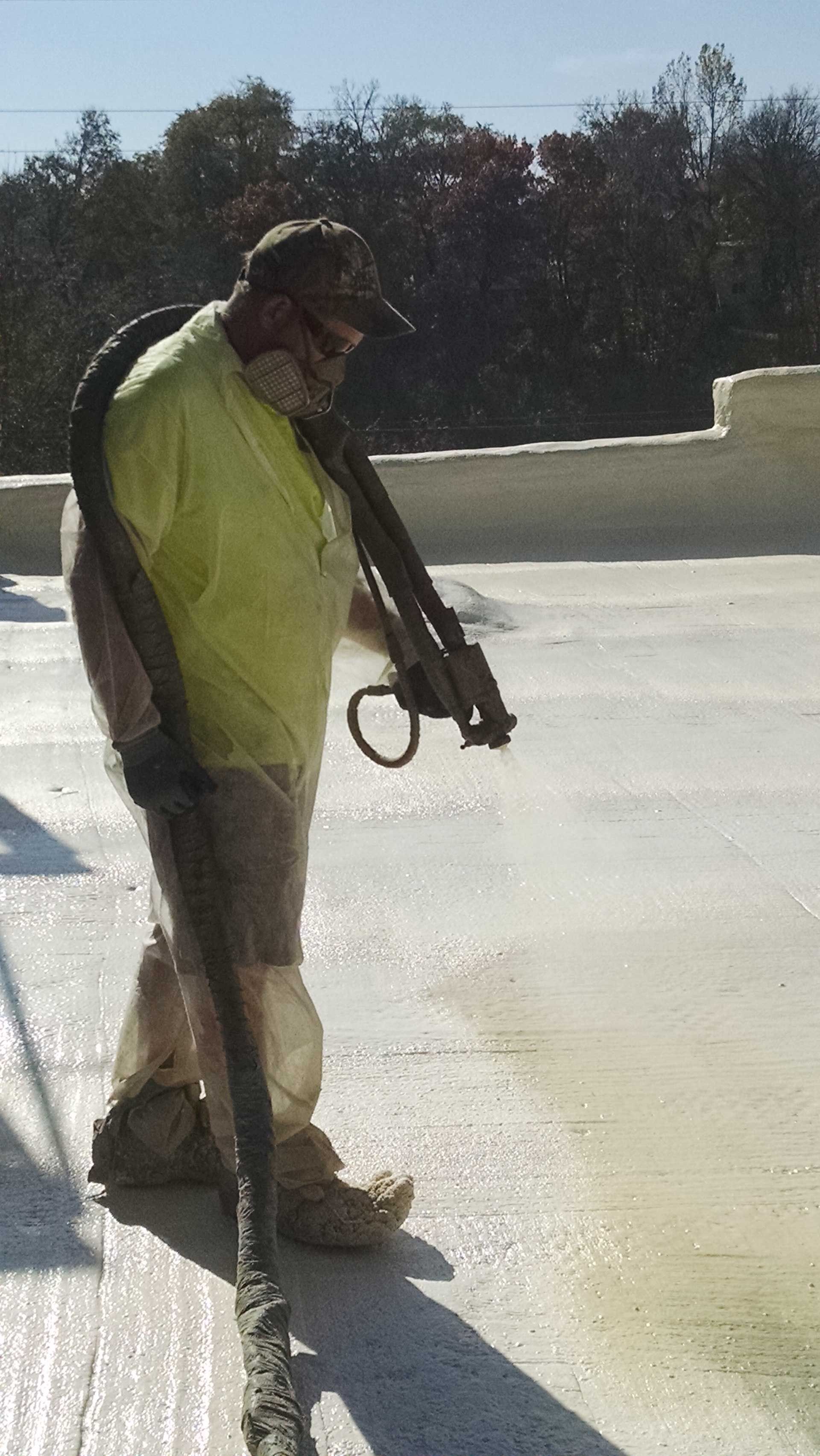 A man spraying foam insulation on a roof, wearing protective gear.