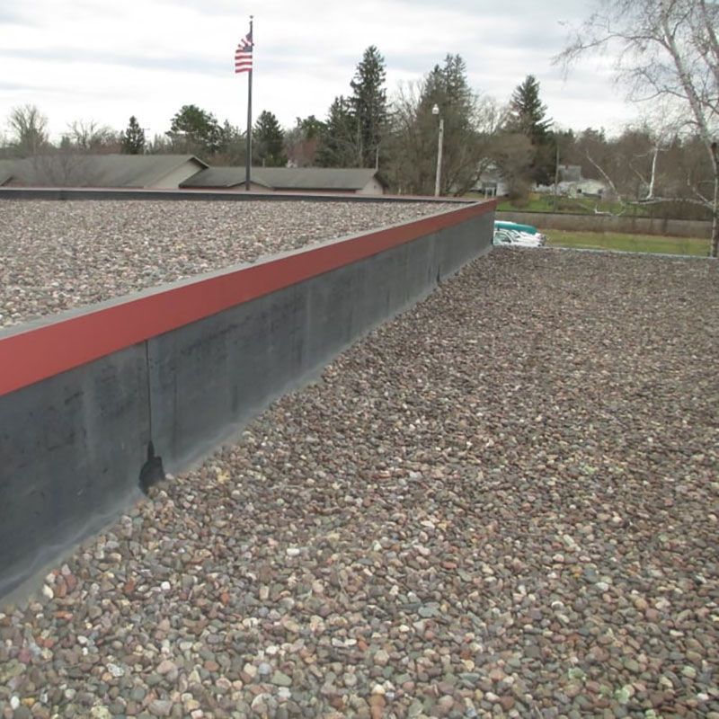 Rooftop with gravel covering, red trim, and American flag on a cloudy day.