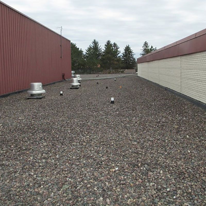 Gravel-covered flat roof between two buildings, one red and one white brick, under a cloudy sky.
