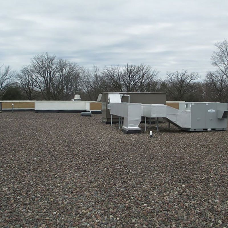 A gravel-covered commercial rooftop with HVAC equipment under a cloudy sky.