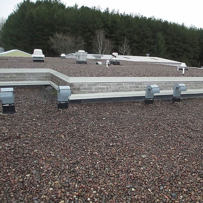 Flat roof covered in small brown stones, vents, and brick facade. Trees in the background.