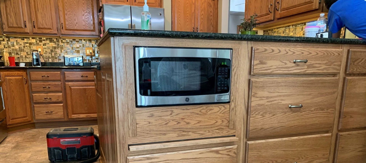 Kitchen island with built-in microwave and drawers; oak cabinets, dark countertop.